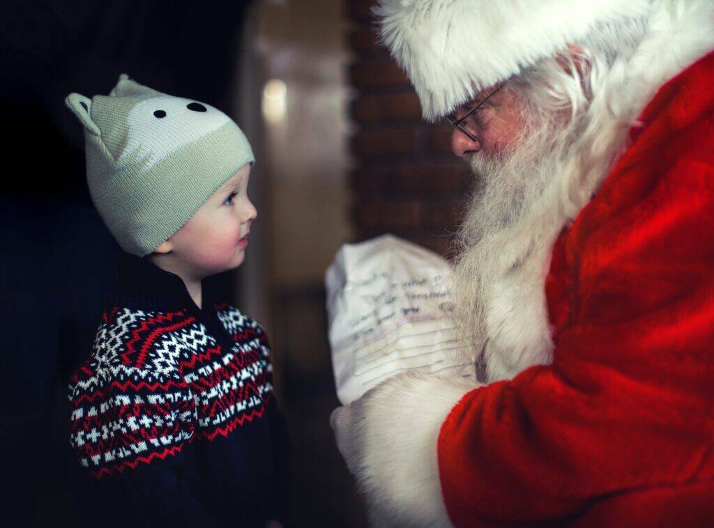 A small child, dressed in festive clothing, meets Santa