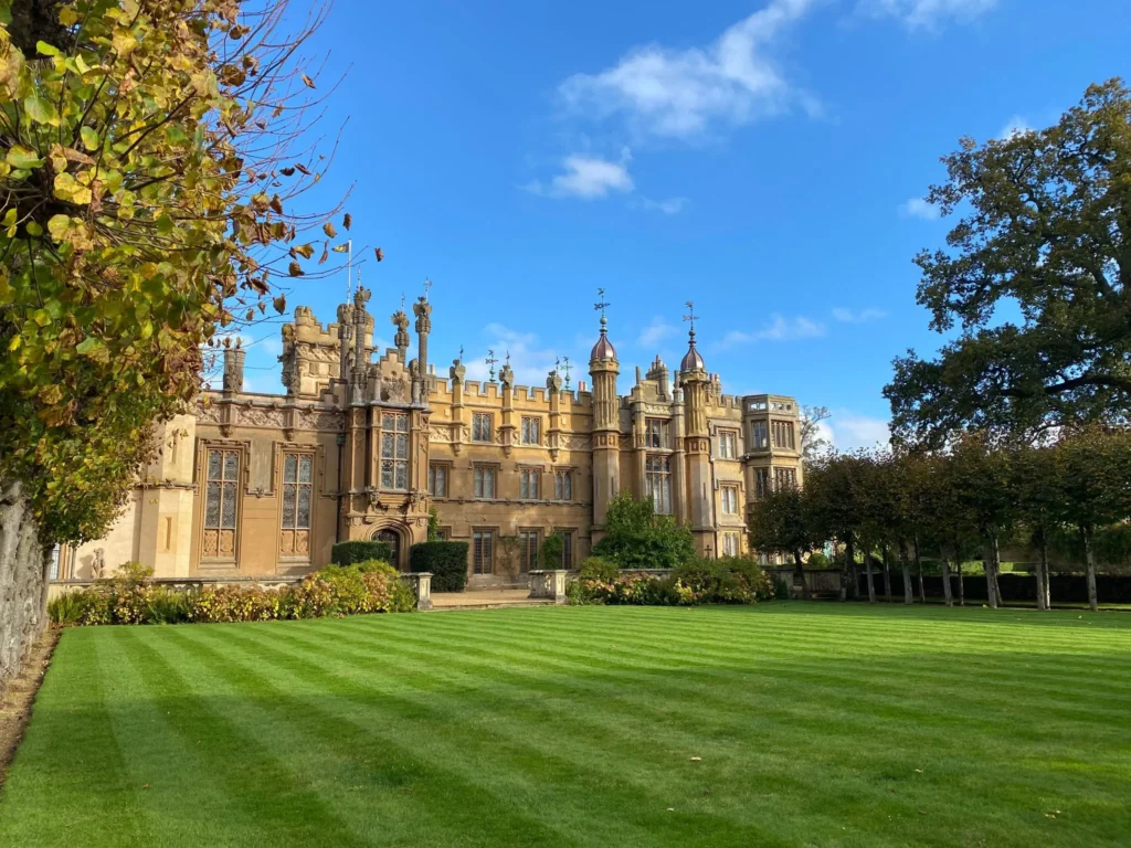 The formal green lawn in front of the historic Knebworth House surrounded by several trees, creating a serene outdoor space.